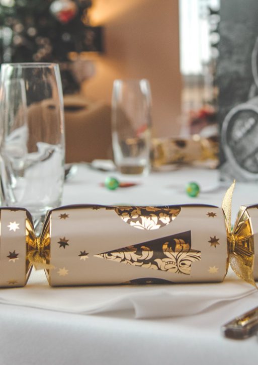 A white, gilded Christmas cracker decorates a covered table.