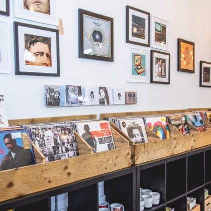 The wall of a record store is lined by framed pictures and shelves of records.