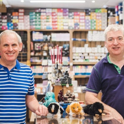 2 Elderly gentlemen pose smiling infront of their products.