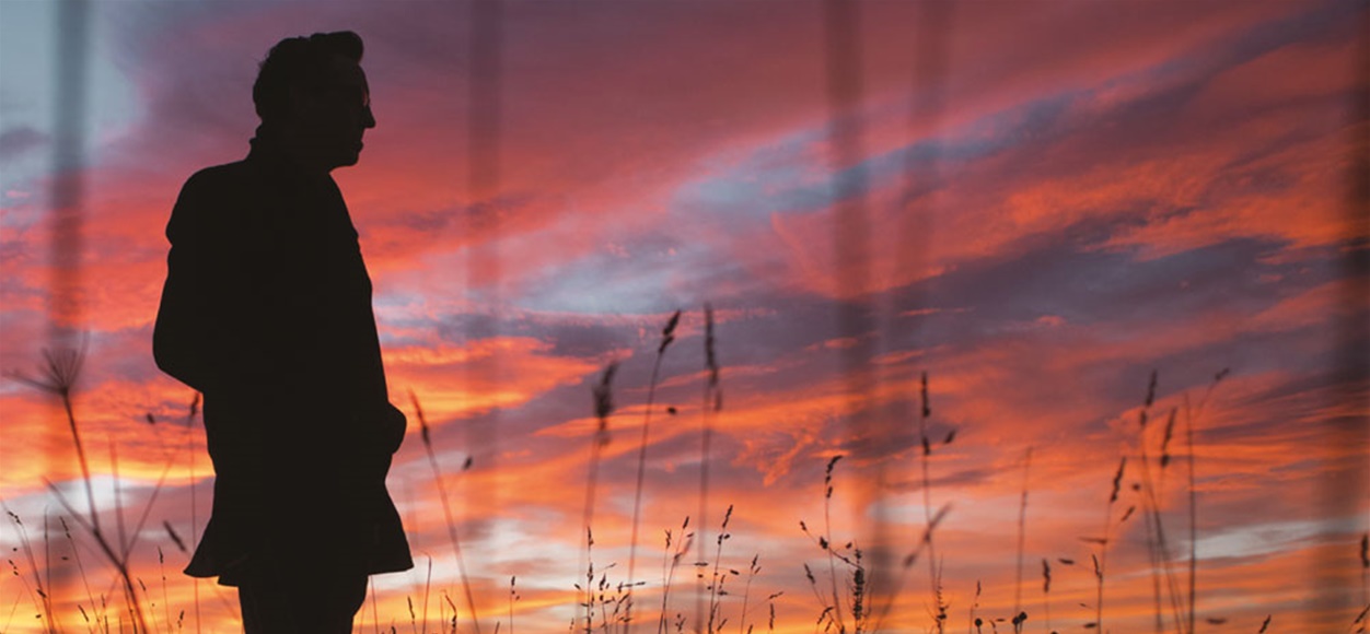 Silhouetted man stands in wheat field at sunset.