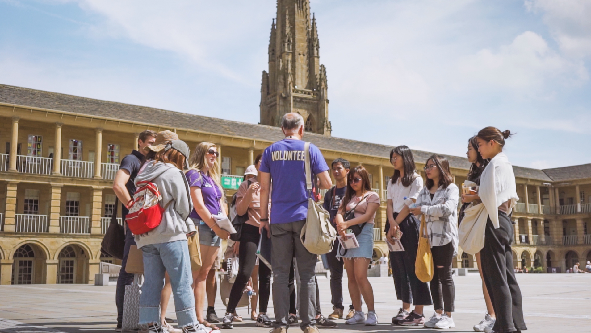 A group of people gather to listen to a man wearing a Volunteer shirt.