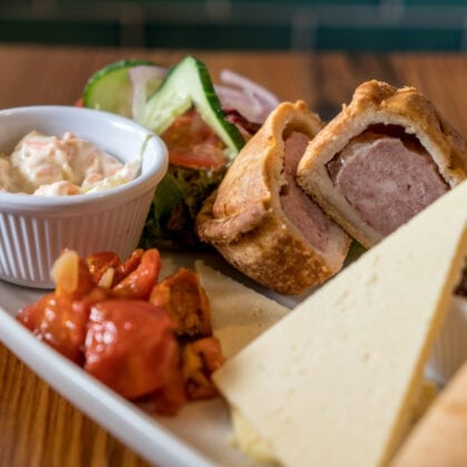 An image of some pub food, with a Pork pie, salad, cheese and coleslaw.